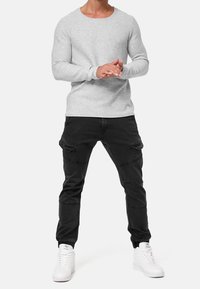 Chemise grise à manches longues avec un col rond, associée à un pantalon cargo noir avec des poches et des chevilles resserrées, complétée par des baskets blanches.