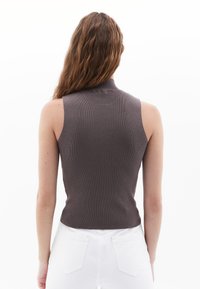 Fitted bezrukávový top v texturované tmavě hnědé tkanině, s vysokým výstřihem a zkráceným střihem. V kombinaci s bílými džínami s vysokým pasem.