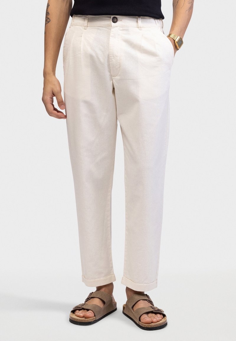 Lichtbeige katoenen broek met plooien, een knoopsluiting en opgerolde broekspijpen. Gecombineerd met bruine sandalen, wat zorgt voor een casual, ontspannen pasvorm.