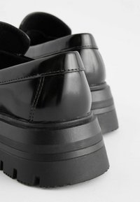 Schwarze Lackleder-Plateauschuhe mit einer dicken, strukturierten Gummisohle und runder Zehenpartie. Mit gesteppten Details entlang der Ferse.