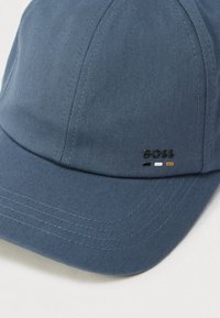 Μπλε καπέλο από υφασμάτινη ύφανση, με καμπύλη κορυφή και ραμμένο σχέδιο. Λογότυπο 'BOSS' με τρία χρώματα τονισμού στο μπροστινό μέρος.