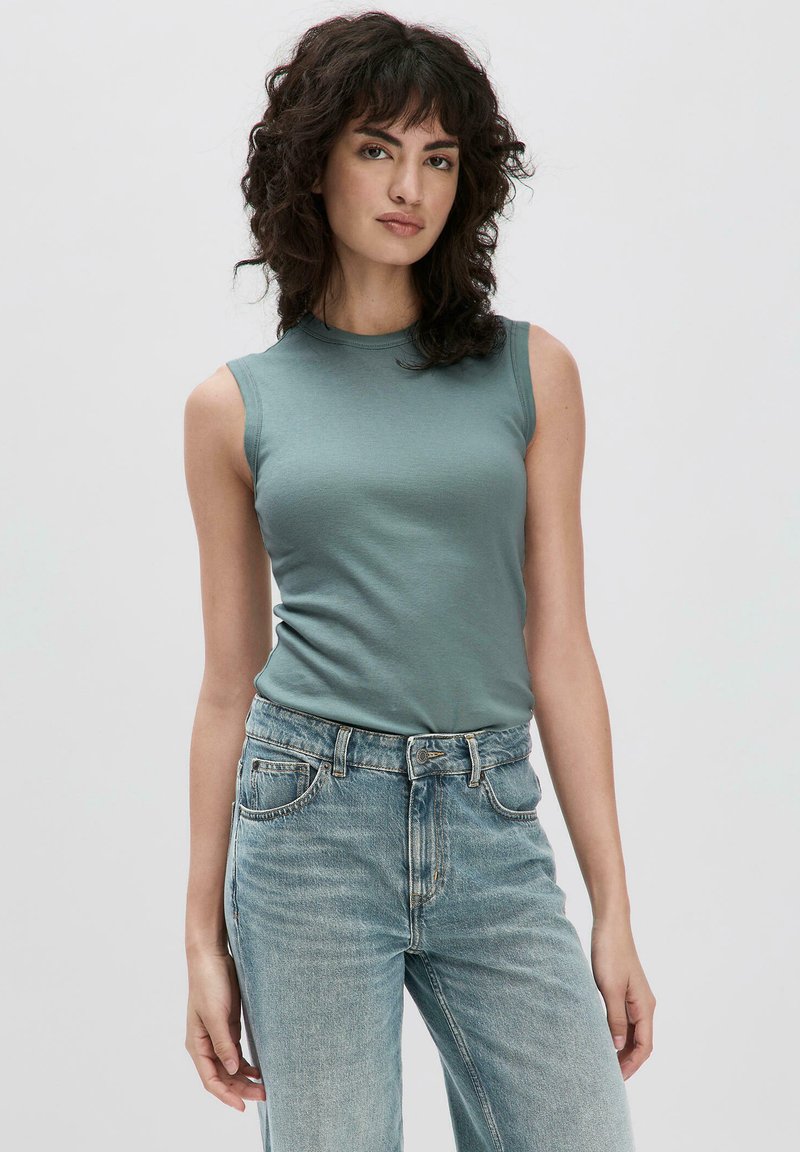 Top sans manches vert en tissu doux, associé à un jean taille haute bleu délavé avec un design classique à cinq poches et une couture visible.