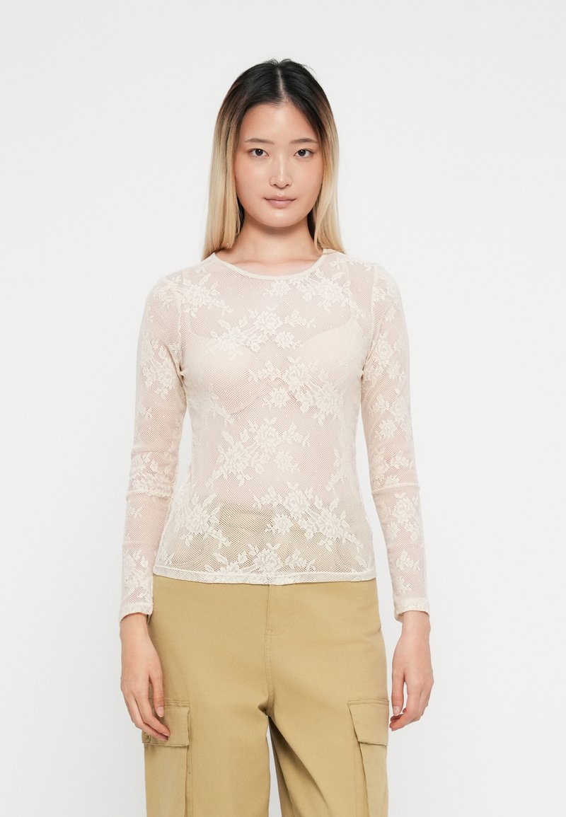 Langermet topp laget av transparent blonde i blush farge, med blomster mønstre og rund hals. Båret med beige cargo bukser.