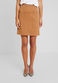 Hnědá mini sukně s texturou a geometrickým vzorem, má přiléhavý střih a rovný lem. Nošena s lodičkami s hadím vzorem a špičatou špičkou.