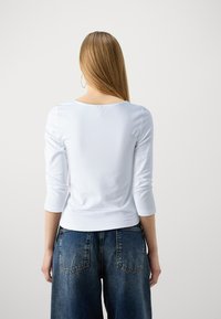 Top bianco a maniche lunghe con scollo rotondo, abbinato a jeans in denim blu dal taglio morbido. Tessuto liscio, vestibilità casual e design minimalista.