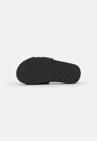 Black rubber shoe sole with a wavy grip pattern. The upper section features soft, textured material in a muted color.