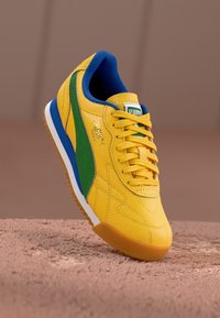 Αθλητικά παπούτσια Puma με κίτρινο δερμάτινο πάνω μέρος, πράσινες και μπλε λεπτομέρειες, υφή, σχέδιο με κορδόνια και καφέ καουτσούκ σόλα.