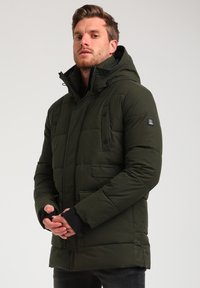 Giacca a vento verde con cappuccio, chiusura con zip e bottoni a pressione. Presenta due tasche anteriori e polsini a coste. Materiale impermeabile, design trapuntato.