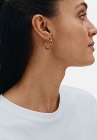 Gold hoop earring on a model, featuring a smooth finish and a circular design, worn in the left ear against a light background.