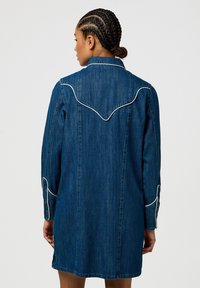 Abito camicia in denim blu scuro con design a yoke in stile western, dettagli in piping bianco e maniche lunghe con bottoni sui polsini.