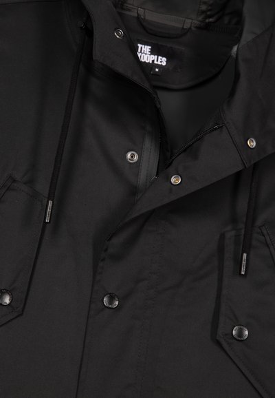 Schwarze Jacke mit Reißverschluss, Druckknöpfen, zwei Fronttaschen und einer verstellbaren Kapuze. Aus einem strukturierten Stoff gefertigt. Markenlabel sichtbar.