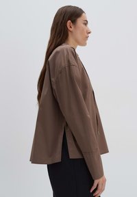 Bruine, langwerpige blouse met een relaxte pasvorm, zijsplitten en een zachte textuur. Heeft een minimalistisch ontwerp en een gestructureerde silhouet.