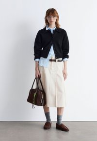 Schwarze Strickjacke, hellblaues Hemd mit Knöpfen, cremefarbene Midirock, braune Handtasche mit Akzenten, graue Socken, braune Slipper. Schlichtes und strukturiertes Design.