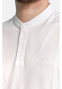 Polo shirt bianca in cotone con collo alla cinese, tre bottoni e logo in rilievo "A/X ARMANI EXCHANGE" sul petto.