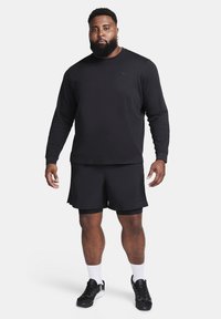 Black long-sleeve Nike shirt paired with black shorts. Features a subtle logo, athletic fit, and worn with black sneakers and white socks.