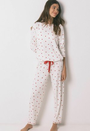 Hvid rippet pyjamasæt med røde hjerte-mønstre, med rund hals, lange ærmer og bukser med elastik i taljen og rød snor.
