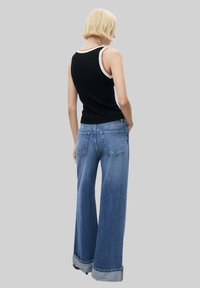Top negru cu dungi, cu margine albă, combinat cu blugi evazați din denim albastru. Blugii au un tiv pliat și două buzunare pe spate.