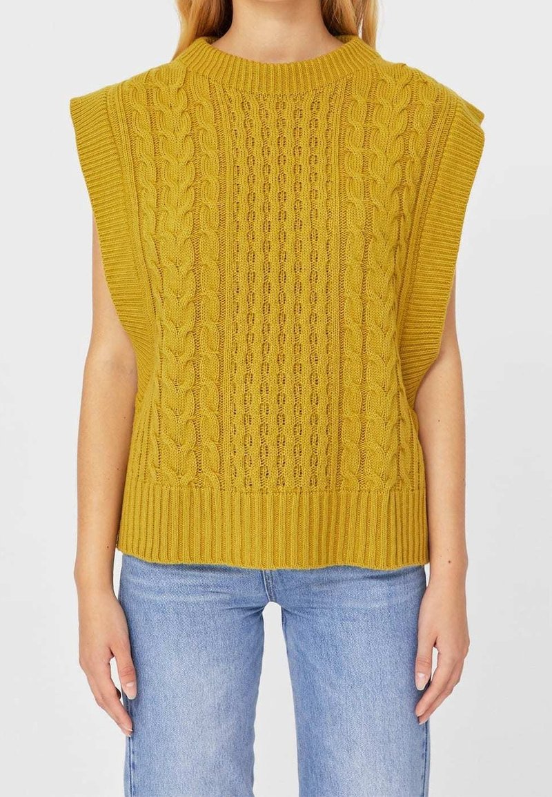 Pull sans manches en tricot jaune moutarde avec un motif torsadé texturé et un ourlet côtelé, associé à un jean bleu clair.