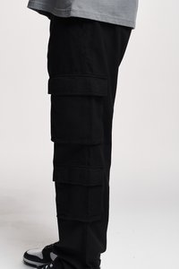 Pantaloni cargo negri cu multiple buzunare laterale, având o croială lejeră și material din bumbac moale. Un tricou gri este parțial vizibil alături.