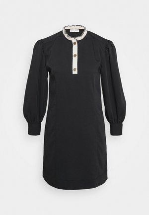 Petite robe noire avec un col montant, manches bouffantes, fermeture à boutons sur le devant et bordure blanche contrastante le long du col. Comprend des boutons décoratifs.