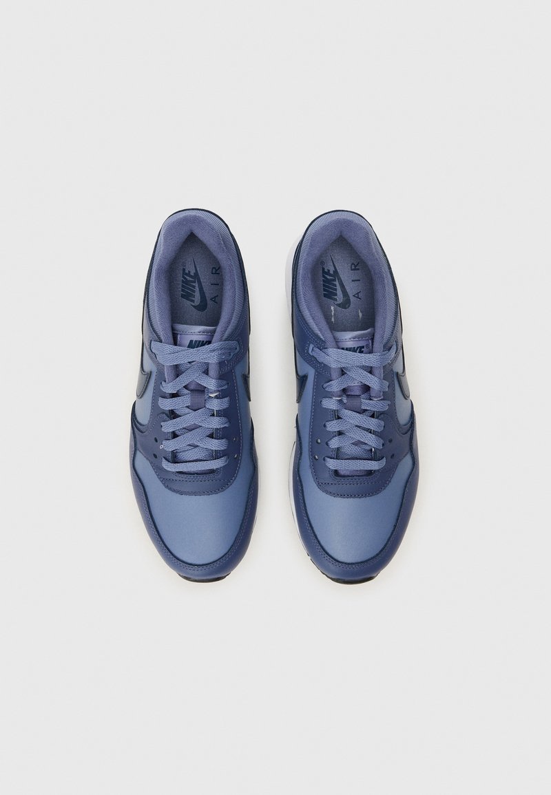 Nike sneakers i forskellige nuancer af blå, med en glat syntetisk overdel, runde snørebånd og en tekstureret sål. Logoet er synligt på tungen.