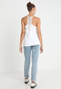 Top bianco senza maniche con dettagli in pizzo sul retro, abbinato a jeans azzurri e scarpe in bianco e nero, caratterizzato da una vestibilità comoda.