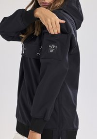 Svart pulloverjacka med huva, med en dragkedjeficka, ribbade ärmslut och en "SLADE COUTURE" logotyp på vänster arm. Slät textur.