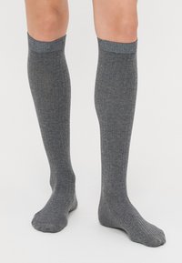 Calze grigie fino al ginocchio con una texture a coste e una banda scura a contrasto nella parte superiore, che mostrano una vestibilità aderente e un tessuto liscio.