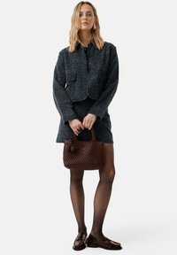 Completo giacca e gonna in tweed blu scuro, abbinato a una borsa intrecciata marrone e scarpe lucide marroni. Gli accessori includono un anello e orecchini.