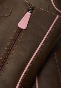 Lähedalt vaadatuna pruun nahk roosa äärise ja tõmblukuga, millel on roosast tilgakujuline tõmbluku tõmbamisnupp.