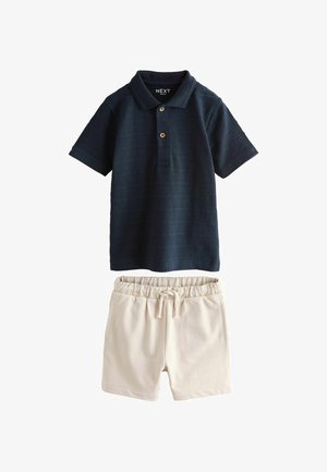 Tumesinise tekstuuriga polosärk kolme nööbiga ja beežid elastse vöökohaga lühikesed püksid. Mõlemad esemed on valmistatud pehmest kangast.