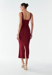Burgundská, priliehajúca midi šaty s vykrojeným chrbtom a bočným rozparkom. Vyznačujú sa hladkou látkou a širokými ramienkami. Nosené s telovými vysokými podpätkami.