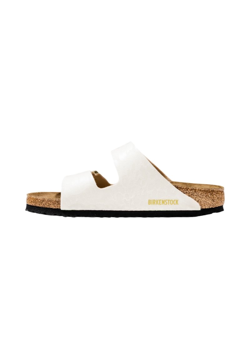 Witte slide-sandaal met dubbele banden, kurken voetbed en gestructureerde bovenkant. Voorzien van een zwarte loopzool met een gouden "Birkenstock"-logo.