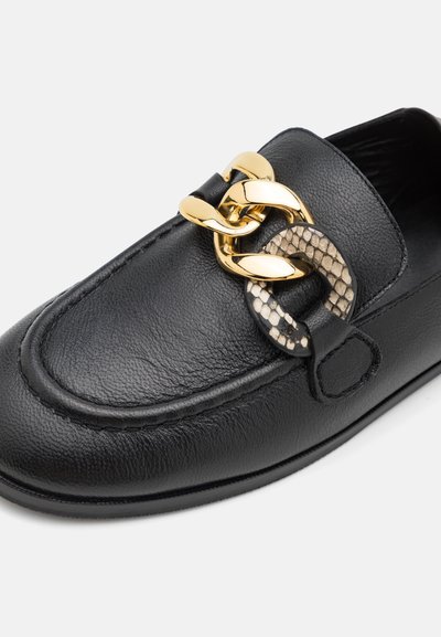 Μαύρη δερμάτινη loafer με υφή, διαθέτει χρυσή αλυσίδα και λεπτομέρεια με σχέδιο φιδιού. Υποδήματα με επίπεδη σόλα και ελάχιστη ραφή.