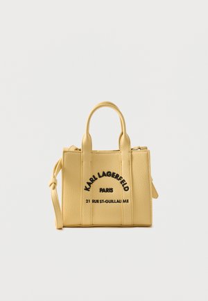 Geantă mică galbenă texturată, cu două mânere, curea detașabilă și text negru „Karl Lagerfeld Paris 21 Rue St-Guillaume” pe față.