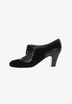 Black high-heeled shoe featuring a combination of suede and shiny leather, with a tied bow detail and cut-out design on the side.