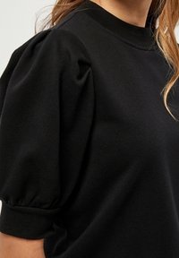 Černá mikina s kulatým výstřihem a krátkými nabíranými rukávy s elastickými manžetami. Tkanina vypadá hladce a odolně.