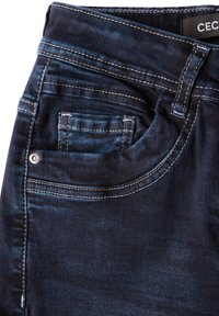 Vaqueros de mezclilla azul oscuro con una textura suave, que presentan costuras blancas contrastantes, un pequeño bolsillo delantero y una cintura estándar.