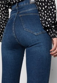 Jeans de tiro alto de color azul oscuro con una textura de denim suave, que cuentan con dos bolsillos traseros y sutiles detalles de costura.