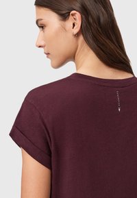 Burgundy t-shirt med kort ärm och uppvikta ärmar, mjuk textur och en liten logodetalj vid nacklinjen. Avslappnad design.