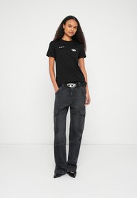 Čierne bavlnené tričko s krátkymi rukávmi a grafickými detailmi, kombinované s voľnými tmavosivými cargo nohavicami a čiernymi lodičkami so špicatou špičkou.