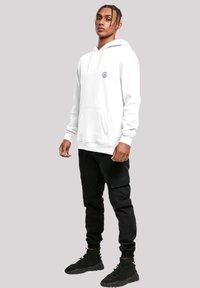 White hoodie with a front pocket and blue logo, paired with black cargo pants and black high-top sneakers. Designed for casual wear.