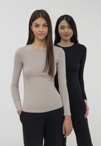 Due magliette a maniche lunghe: una in beige chiaro e l'altra in nero. Entrambe hanno un design aderente e scolli rotondi, realizzate in un tessuto lisso.