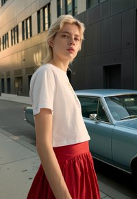 Hvit kort t-skjorte med grafisk trykk, kombinert med en lang, flytende rød skjørt. Bakgrunnen viser en vintage blå bil og moderne bygninger.