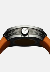 Buntes Armbanduhrenmodell mit einem Edelstahlgehäuse, graviertem geometrischem Muster, orangefarbenem Gummiband und einer runden Krone mit einem Emblem.