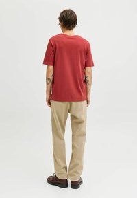 Rød bomulds t-shirt med korte ærmer, afslappet pasform, båret med beige lige ben bukser og brune snørebåndssko. Enkelt design, ingen mønstre.