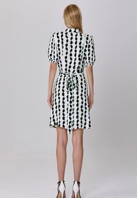 Robe blanche avec un motif de pois verticaux noirs et verts, manches courtes bouffantes, ceinture à la taille et jupe évasée. Texture de tissu lisse.