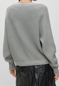 Grauer Strickpullover mit geripptem Saum und Bündchen. Besitzt einen hellrosa Akzent am Halsausschnitt. Weicher Stoff und lockere Passform.