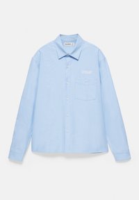 Chemise bleu clair à manches longues boutonnée avec col, poche poitrine et petit texte blanc brodé au-dessus de la poche.