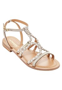 Sandal in pelle beige con cinturini intrecciati, punta aperta, tacco piatto e chiusura alla caviglia. Presenta una suola liscia e accenti hardware minimi.
